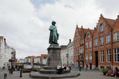Bruges, Belgium - September 13, 2022: Overall view of the small square on which the painter Jan van Eyck memorial by Jan Calloigne is situated. There are townhouses on the canal in the backgroun