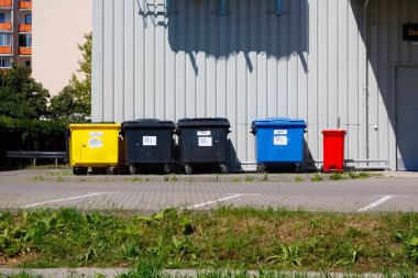 Warsaw, Poland - August 7, 2022: Waste sorting bins have been placed against a metal wall at the back of the store and next to empty parking spaces