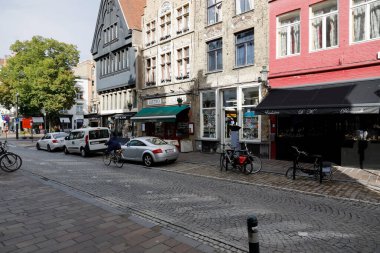 Bruges, Belgium - September 8, 2022: A narrow cobblestone street with parking spots for cars and bicycles runs past brick houses with visible shop window