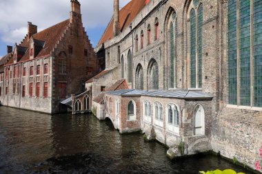 Bruges, Belgium - September 11, 2022: Large, brick building of Johns Hospital is located on the canal. There are massive brick walls, huge windows of the building, which dates back to the Middle Ages.