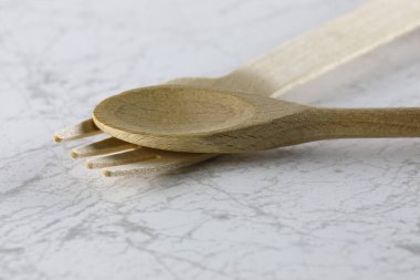 One spoon and one fork made of natural material such as wood have been placed on a marble countertop