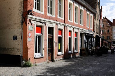 Bruges, Belçika - 15 Eylül 2022: Dar kaldırımlı bir cadde boyunca geniş pencereli eski bir tuğla evin cephesi görülüyor. Yanında da diğer tuğlalardan evler var.