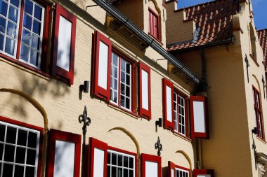 Bruges, Belçika - 11 Eylül 2022: Sarı tuğla ev güneşli bir günde burada görülen kırmızı ve beyaz renklere boyanmış pencere ve panjurlarla donatılmıştır. Artık orada kimse yok.
