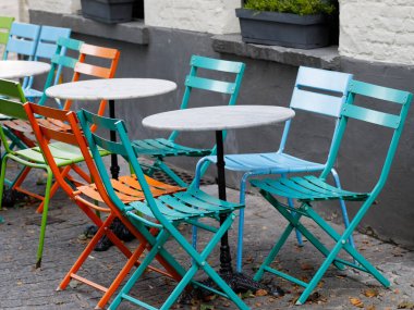 Açık bir kafe veya restoranda sandalye ve masalar boş duruyor ve misafirleri bekliyor..