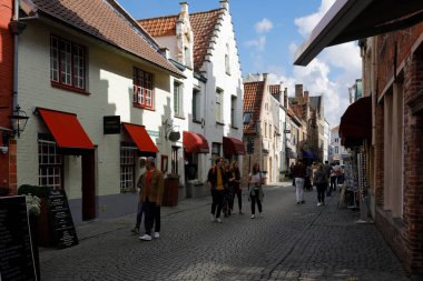 Bruges, Belçika - 11 Eylül 2022: Tuğla binalar bu harika ortaçağ şehrinin parke taşı caddesi boyunca görülebilir. Burada insanlar sokakta yürüyor.