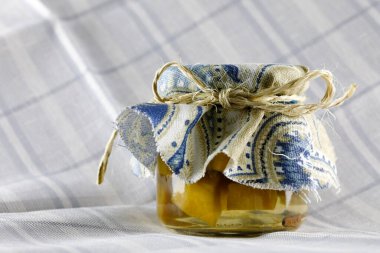 A glass jar with preserves topped with a piece of cloth and rolled up with a twine.