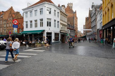 Bruges, Belçika - 7 Eylül 2022: Tarihi evler, kaldırımlı caddeler, açık hava restoranı, çok sayıda insan var, yaya geçidinde caddeleri geçen biri,