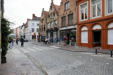 Bruges, Belçika - 10 Eylül 2022: Eski kasabada kaldırımlı bir cadde ile yaya geçidi arasında eski, tarihi tuğla binalar var. Orada birkaç kişi var.