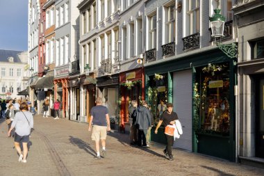 Bruges, Belçika - 10 Eylül 2022: İnsanlar zeminde birçok mağaza önü bulunan çeşitli evlerin yakınındaki kaldırım kaldırımlarında yürüyor