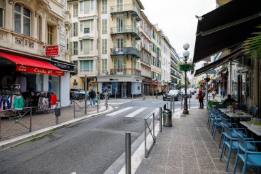 Güzel, Fransa - 29 Nisan 2023: her iki tarafında vitrinler olan şehir caddesi. Ayrıca mavi sandalyeleri görünen bir kaldırım restoranı da var.