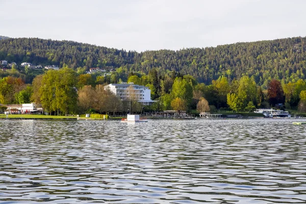 Velden Am Worthersee, Avusturya - 4 Mayıs 2023: Güzel doğanın yakınlarındaki evlere doğru göl manzarası burayı büyük bir tatil beldesi haline getiriyor