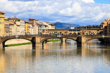 Florence, İtalya - 15 Nisan 2023: Arno nehri boyunca uzanan iki köprü. Nehir kıyısında görünür konutlar var. Uzakta bir tepe var.