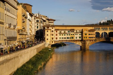 Floransa, İtalya - 16 Nisan 2023: Arno Nehri kıyısındaki eski kasabanın binaları ve Ponte Vecchio 'nun bir kısmı akşam güneşinin yavaşça batmasıyla aydınlanır.