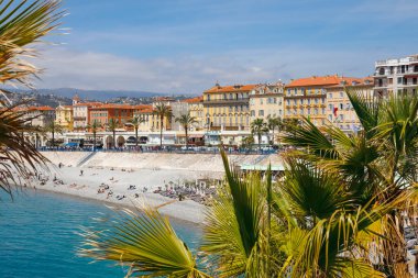 Nice, Fransa - 28 Nisan 2023 Akdeniz kıyısı boyunca ve şehirdeki binalar boyunca bir plaj. Sahilde deniz kenarındaki cazibe ve manzaranın tadını çıkaran insanlar var..