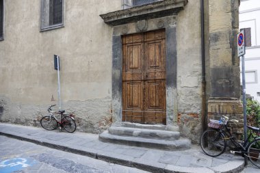 Floransa, İtalya - 17 Nisan 2023: büyük tuğla bir binaya devasa bir ahşap kapı. Binanın duvarına iki bisiklet park edilmişti.