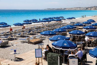 Güzel, Fransa - 26 Nisan 2023: güneşli bir günde, Akdeniz sahillerine koyu mavi şemsiyeler yayıldı. Şemsiyelerin gölgesinde deniz kenarındaki güzelliklerden hoşlanan insanlar var.