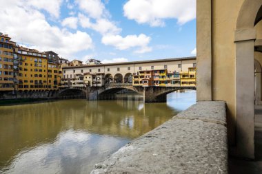 Florence, İtalya - 15 Nisan 2023: Arno Nehri boyunca uzanan ortaçağ Ponte Vecchio (Eski Köprü). Bir grup insan uzaktaki köprüde görülebilir.