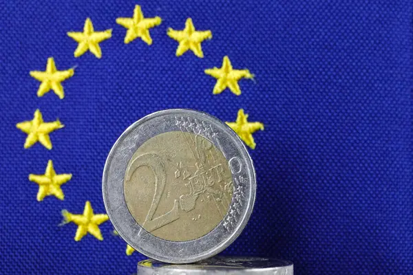 ここに示されている硬貨は 黄色い星の円を持つ青いヨーロッパの旗に対して示されている欧州連合の通貨です この写真は さまざまな金融問題の背景となり得る — ストック写真