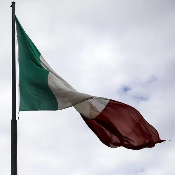 The national flag of Italy is placed at the top of the flagpole and there it waves in the wind and is visible against a cloudy sky in Florence, Italy
