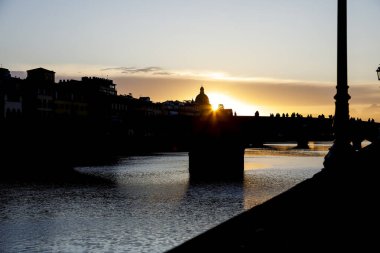 Arno nehri boyunca uzanan eski köprünün üzerindeki yaz günbatımının manzara manzarası. İtal 'da Floransa şehrinin renkli günbatımı gökyüzüne karşı köprü ve binalar görülebilir.