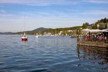 Velden Am Worthersee, Avusturya - 4 Mayıs 2023: Göl manzarası ve tekneler demirli. Gölün kıyısında açık hava restoranı var.