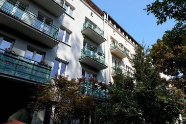 Varşova, Polonya - 12 Eylül 2023: Ağaçların arasında Praga-Poludnie bölgesinin bir parçası olan Saska Kepa konutlarında güneş ışığıyla yıkanmış bir apartman bloğu var..