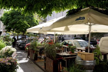 Varşova, Polonya - 20 Eylül 2023: Masalar şemsiyelerle gölgelendi ve doğa tarafından çevrildi. Burası şehir merkezindeki bir caddenin kaldırımında açık hava restoranı..