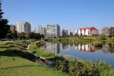Varşova, Polonya - 18 Eylül 2023: Praga Poludnie bölgesindeki Goclaw konutlarında çok katlı apartman blokları ve bir kiliseyle birlikte var olan bir göl.
