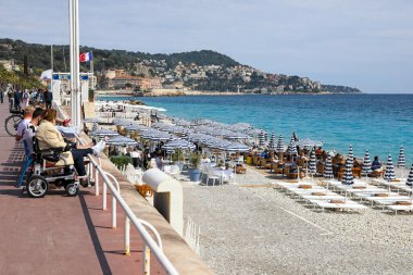 Güzel, Fransa - 21 Nisan 2023: Güneş banyosunun güneşlenebileceği bir çakıl taşı plajında mavi-beyaz şemsiyeli bir plaj.