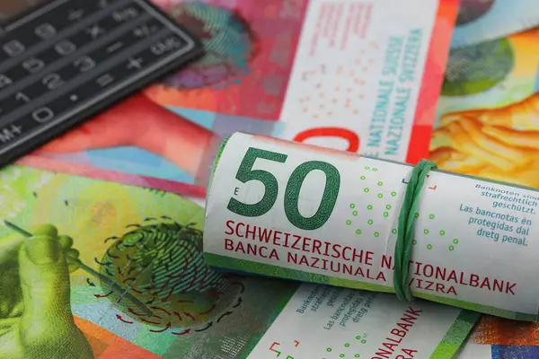 A roll of Swiss franc banknotes, other Swiss paper money and a calculator. CHF paper money. This theme can be used to illustrate many different financial topics.