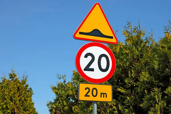 stock image The yellow sign warning of a bump in the road to slow down traffic in 20 metres. This is followed by a round road sign with a red border, a white centre and a black number 20, which limits the speed to 20 km/h