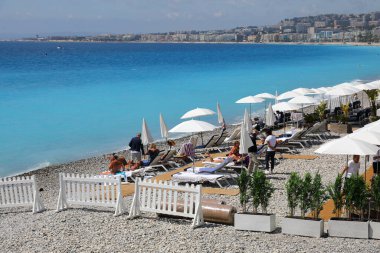Güzel, Fransa - 26 Nisan 2023: Güneş banyosu yapanların güneşlenebilmesi için çakıl taşlı plajda beyaz şemsiyeler ve güneşli yataklar