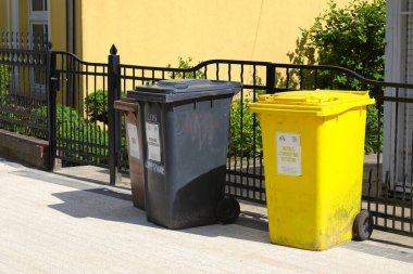 Ustronie Morskie, Polonya - 29 Mayıs 2024: Üç farklı renkte üç çöp bidonu kaldırıma, mülkün metal çitlerine karşı yerleştirildi