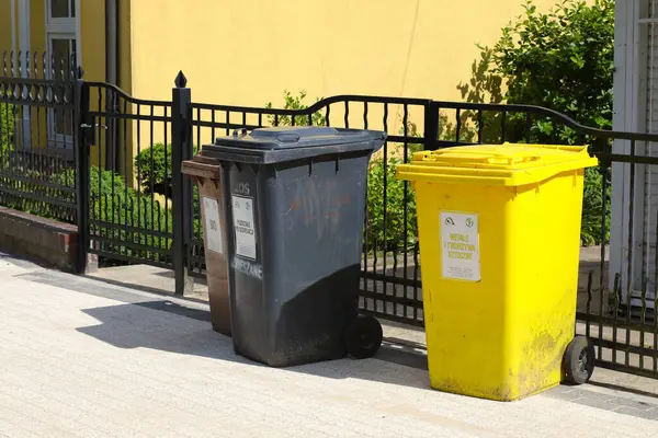 Ustronie Morskie, Polonya - 29 Mayıs 2024: Üç farklı renkte üç çöp bidonu kaldırıma, mülkün metal çitlerine karşı yerleştirildi