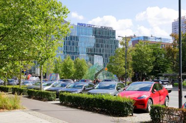 Varşova, Polonya - 1 Eylül 2023: Cam cepheli modern bir bina. Şehir merkezinde bir sürü ağaç ve park edilmiş araba var..