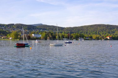 Velden Am Worthersee, Avusturya - 4 Mayıs 2023: Gölün karşısındaki ağaçlık tepeler ve güzel kırsal kesimin merkezindeki evler ile burası tatil için harika bir yer.