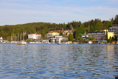 Velden Am Worthersee, Avusturya - 4 Mayıs 2023: Göl, ormanlık tepeler ve güzel kırsal kesimdeki göl evleri burayı tatil için harika bir yer haline getiriyor.