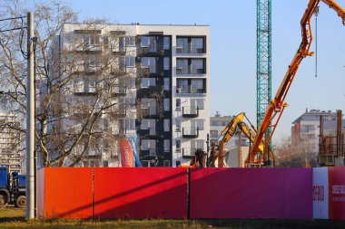 Varşova, Polonya - 30 Ocak 2024: Kırmızı çitin ötesinde yeni evler inşa ediliyor. Biraz ileride Praga-Poludnie bölgesindeki Goclaw konutlarında yeni tamamlanmış bir apartman bloğu var.