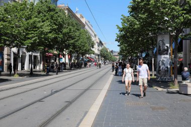 Nice, Fransa - 3 Mayıs 2023: Şehrin ortasında tramvay rayları, her iki tarafında ağaçlar ve şehir mimarisi ve yürüyen insanlar olan düz bir yol