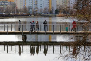 Varşova, Polonya - 18 Şubat 2024: Praga-Poludnie bölgesindeki Goclaw konutlarında karsız bir kış mevsiminde, insanlar gölün üzerindeki yaya köprüsünde ayakta duruyorlar.