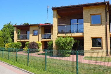 Ustronie Morskie, Polonya - 21 Mayıs 2024: Güneşli bir günde yeşil çitlerin arkasındaki sarı tuğlalı tatil evlerini görebilirsiniz..
