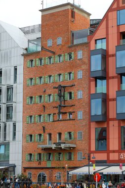 Gdansk, Polonya - 10 Ekim 2024: Duvarında vinç tesislerinin kalıntıları ve yeşil panjurlu küçük pencerelerle eski bir tuğla ve yeniden inşa edilmiş binanın cephesi