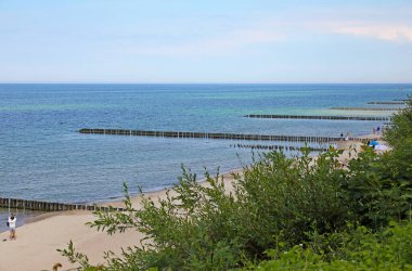 Ustronie Morskie, Polonya - 30 Mayıs 2024: Baltık Denizi kıyısındaki sahil yüksek sezondan önce oldukça sakindir, kalabalık yoktur. Denizde, kumsalın yanında dalgalar ve bitki örtüsü var..