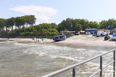 Ustronie Morskie, Polonya - 21 Mayıs 2024: Bu tatil köyünde, bir balıkçı limanı, bir balıkçı teknesi, kıyıdan biraz uzakta balık kızartıcıları, kumlu bir plaj ve ağaçlar görebilirsiniz..