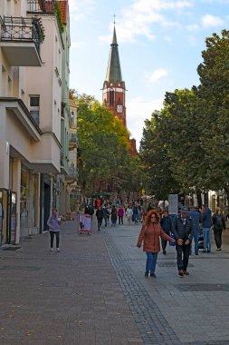 Sopot, Polonya - 7 Ekim 2024: Güneşli bir günde, sanki gölgede gizlenmiş gibi şehrin ünlü gezinti alanı, kilise kulesi ve ağaçlar güneş ışığıyla aydınlatılıyor..