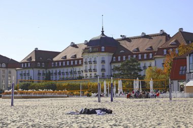 Sopot, Polonya - 12 Ekim 2024: 5 yıldızlı Sofitel Grand Sopot Oteli Gdansk Körfezi 'nin kumlu sahilinin kenarında yer almaktadır. Otel binası 1927 'den kalma. İnsanlar sahilde dinleniyor.