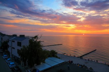 Ustronie Morskie, Polonya - 25 Mayıs 2024: Baltık Denizi plajı boyunca apartman blokları gün batımında koyu gölgede görülebilir. Batan güneş gökyüzündeki bulutları lekeliyor ve denizdeki renklerini yansıtıyor..