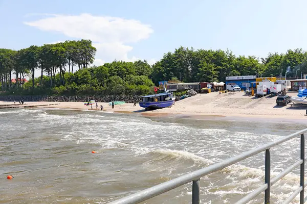 Ustronie Morskie, Polonya - 21 Mayıs 2024: Bu tatil köyünde, bir balıkçı limanı, bir balıkçı teknesi, kıyıdan biraz uzakta balık kızartıcıları, kumlu bir plaj ve ağaçlar görebilirsiniz..