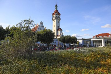 Sopot, Polonya - 12 Ekim 2024: Ülkenin kuzey kesimindeki kıyı kenti binaları Tri-City 'de toplanıyor. Bir gözlem kulesi var, yemyeşil bitki örtüsünün arkasında bir deniz feneri..