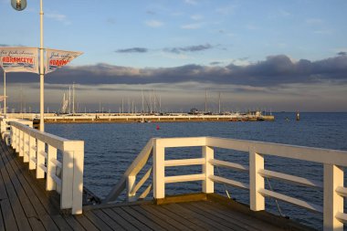 Sopot, Polonya - 7 Ekim 2024: Baltık Denizi kıyısında büyük bir iskele boyunca beyaz ahşap bariyerler. Uzaktan bir marina görülebilir..